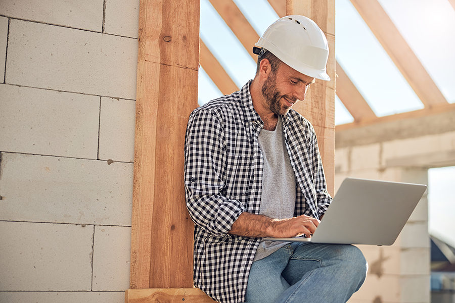 Handsome young man in a hard hat looking at laptop screen while sitting outside the construction site